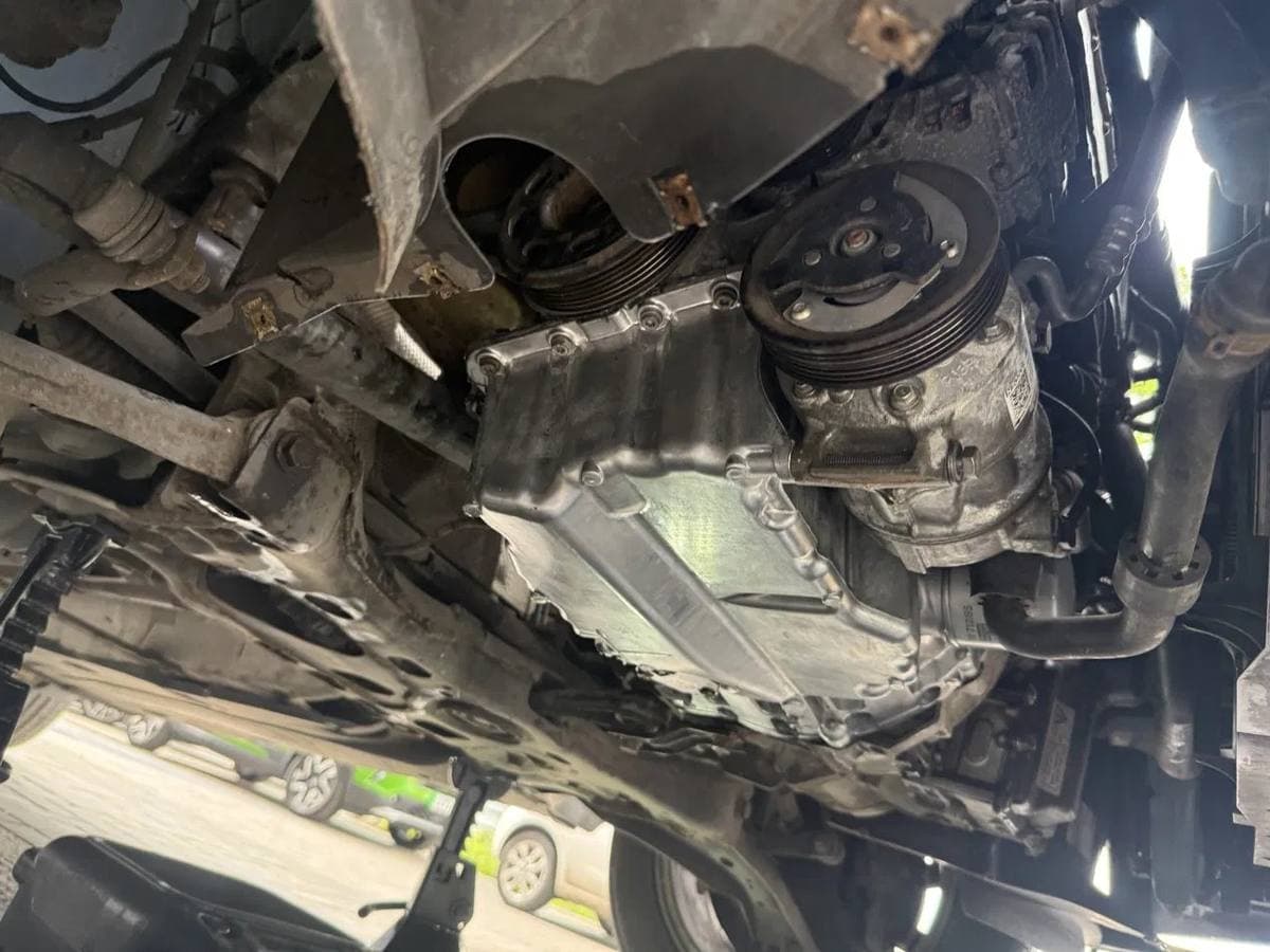 Underside engine bay work on the oil pan and air conditioning compressor